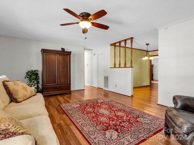 living room with ceiling fan with notable chandelier, crown molding, wood-type flooring, and a textured ceiling