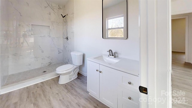 bathroom with hardwood / wood-style floors, vanity, toilet, and a tile shower