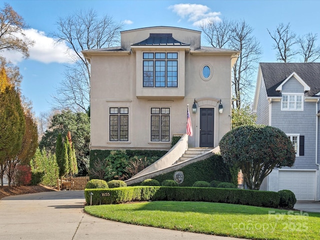 view of front of home featuring stucco siding, driveway, a standing seam roof, a front yard, and metal roof