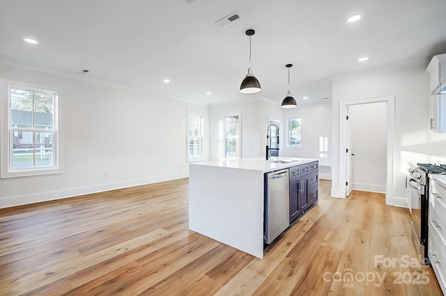 kitchen with a kitchen island with sink, white cabinets, appliances with stainless steel finishes, decorative light fixtures, and light hardwood / wood-style floors