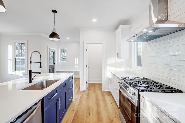 kitchen with wall chimney exhaust hood, stainless steel appliances, blue cabinets, pendant lighting, and white cabinets