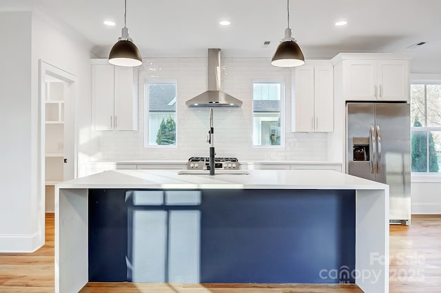 kitchen featuring white cabinets, stainless steel fridge, pendant lighting, and wall chimney range hood