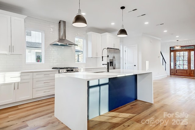 kitchen featuring pendant lighting, white cabinetry, wall chimney range hood, and an island with sink