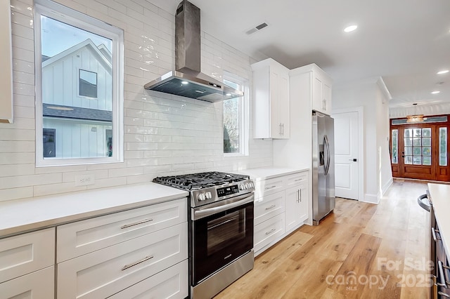 kitchen with light hardwood / wood-style floors, white cabinetry, wall chimney range hood, and appliances with stainless steel finishes