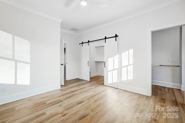 unfurnished bedroom featuring ceiling fan, a barn door, a spacious closet, ornamental molding, and a closet