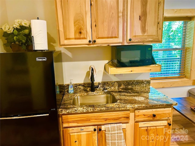 kitchen featuring hardwood / wood-style floors, fridge, dark stone counters, and sink