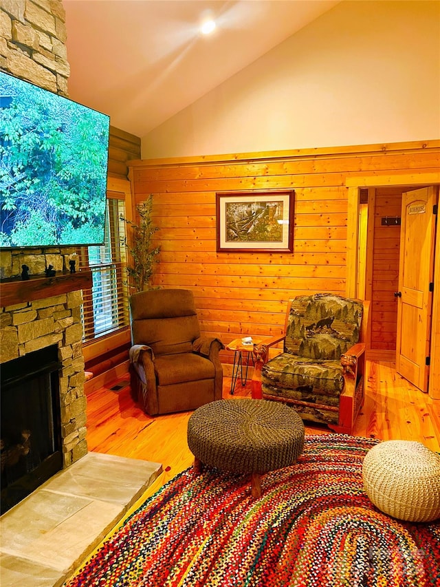 living room with hardwood / wood-style flooring, wood walls, a stone fireplace, and high vaulted ceiling