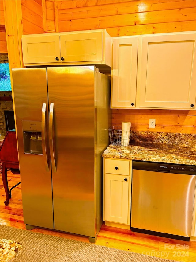 kitchen featuring dark stone countertops, white cabinetry, stainless steel appliances, and wooden walls