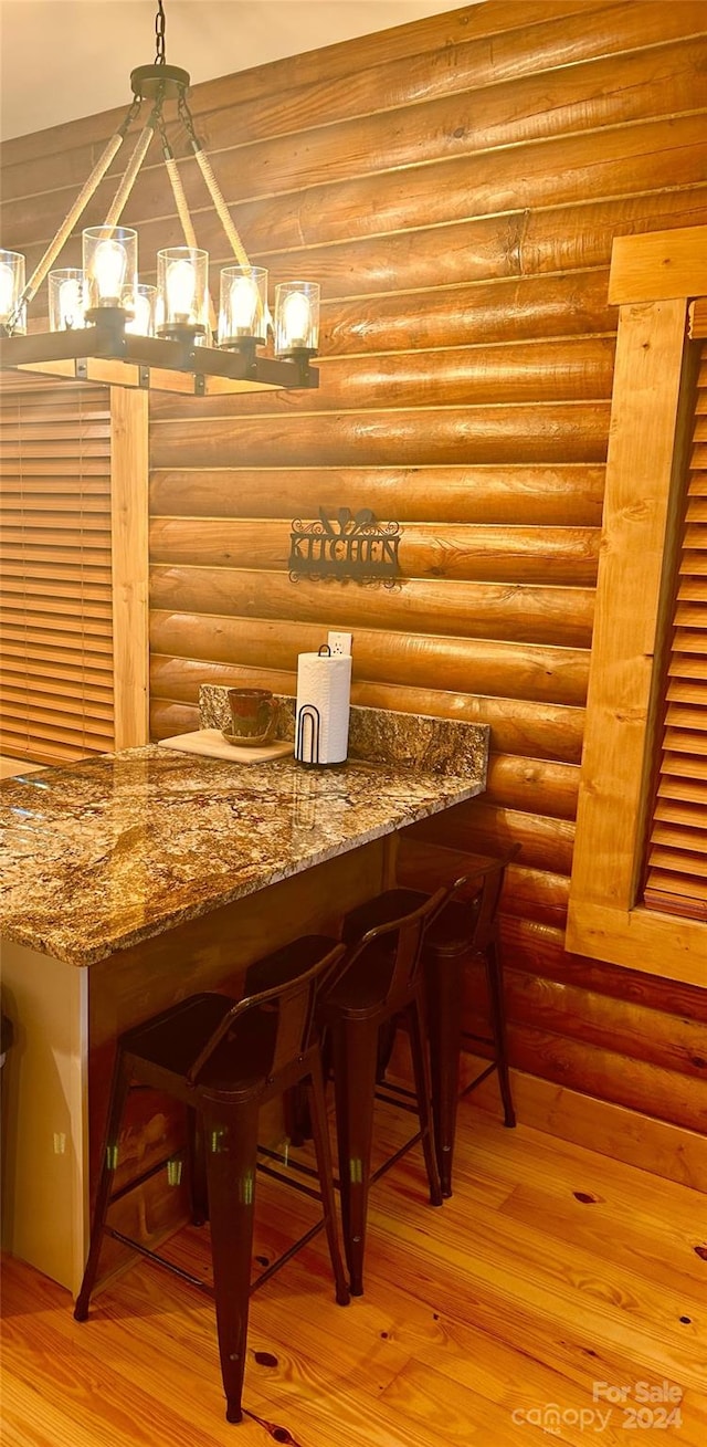 dining area with light wood-type flooring, log walls, and an inviting chandelier