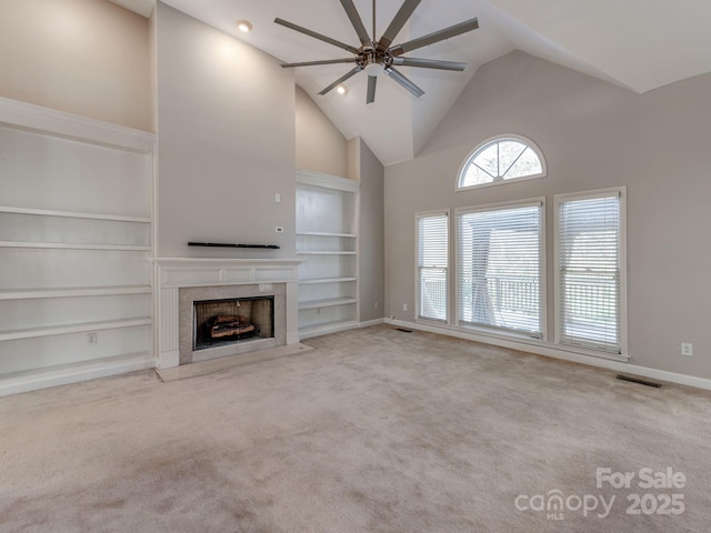 unfurnished living room featuring a high end fireplace, light carpet, built in shelves, high vaulted ceiling, and ceiling fan