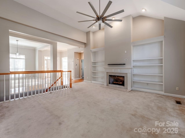 unfurnished living room with crown molding, a high ceiling, built in shelves, a fireplace, and carpet floors