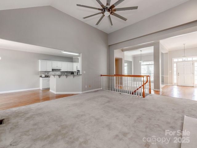 unfurnished living room with crown molding, ceiling fan with notable chandelier, light colored carpet, and lofted ceiling