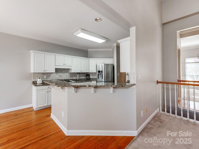 kitchen with white cabinetry, dark stone countertops, kitchen peninsula, backsplash, and stainless steel fridge