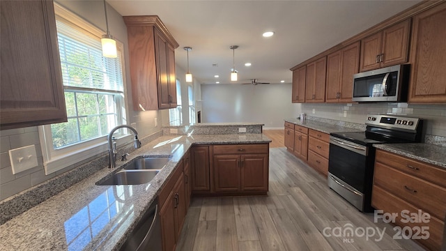 kitchen with a peninsula, a sink, appliances with stainless steel finishes, brown cabinets, and pendant lighting