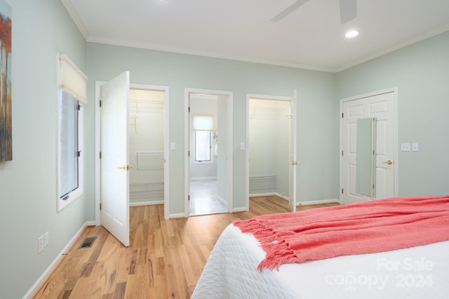 bedroom with connected bathroom, a spacious closet, ceiling fan, crown molding, and light wood-type flooring