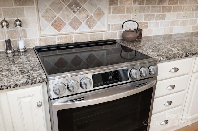 kitchen featuring backsplash, dark stone countertops, white cabinetry, and high end stainless steel range oven