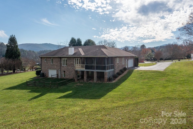 rear view of house with a mountain view, a sunroom, a garage, and a lawn