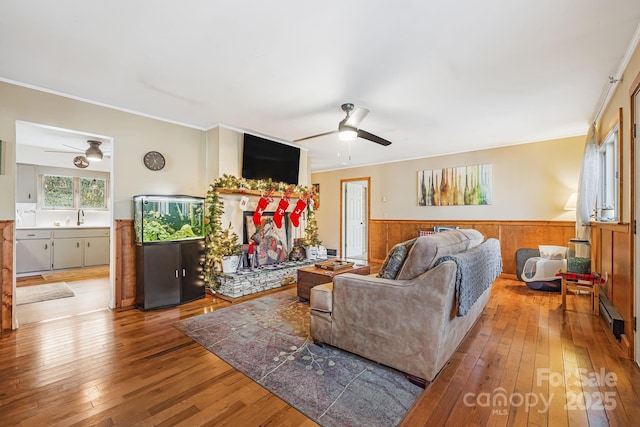 living room featuring ceiling fan, ornamental molding, sink, and light hardwood / wood-style flooring