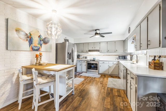 kitchen featuring dark wood-type flooring, decorative backsplash, gray cabinets, appliances with stainless steel finishes, and brick wall