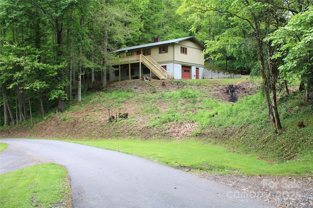 view of front facade featuring driveway, a view of trees, a garage, stairway, and a chimney