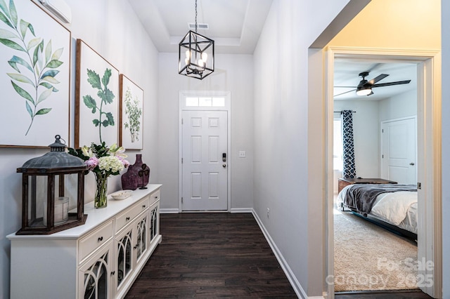 foyer entrance featuring ceiling fan with notable chandelier, dark wood finished floors, visible vents, and baseboards