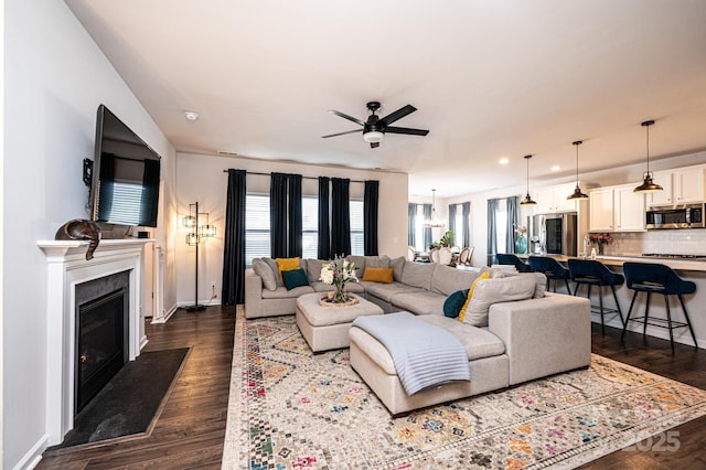 living room with baseboards, a fireplace with flush hearth, ceiling fan, dark wood-style flooring, and recessed lighting