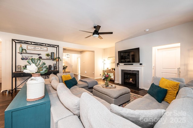 living room featuring ceiling fan, a fireplace with flush hearth, dark wood finished floors, and baseboards