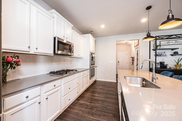 kitchen with a sink, white cabinetry, appliances with stainless steel finishes, backsplash, and dark wood finished floors