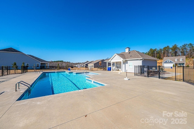 pool with a patio area, fence, and an outbuilding