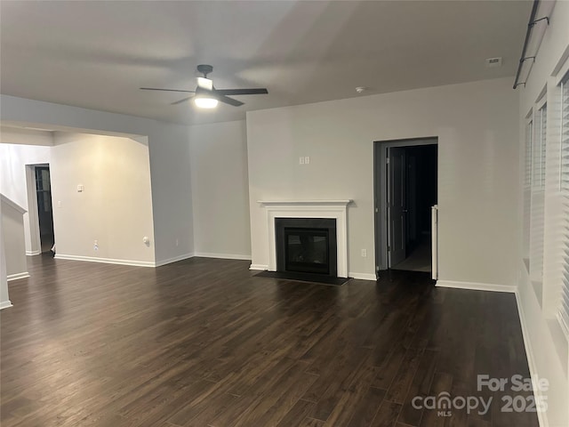 unfurnished living room featuring dark wood-style floors, a fireplace with flush hearth, baseboards, and ceiling fan