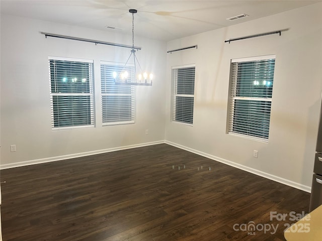 empty room with a chandelier, visible vents, baseboards, and wood finished floors