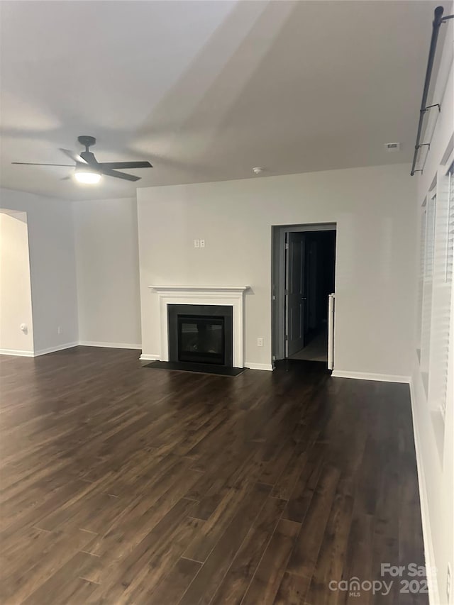 unfurnished living room with ceiling fan, baseboards, dark wood-type flooring, and a glass covered fireplace