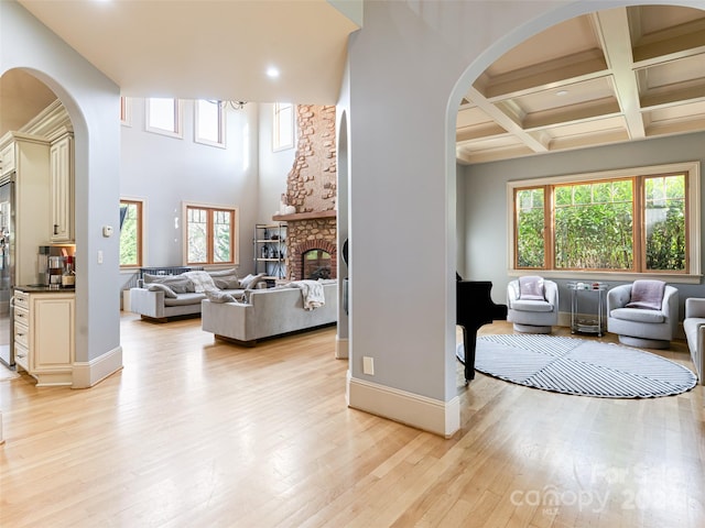 living room featuring a towering ceiling, a brick fireplace, coffered ceiling, beamed ceiling, and light hardwood / wood-style floors