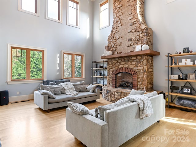 living room featuring a high ceiling, light hardwood / wood-style flooring, and a stone fireplace