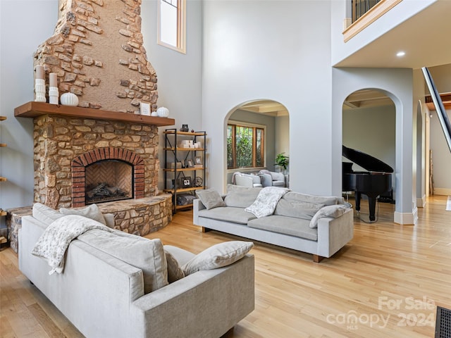 living room with a stone fireplace, a towering ceiling, and light hardwood / wood-style flooring