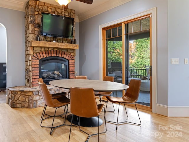 dining space featuring ceiling fan, ornamental molding, a fireplace, and light hardwood / wood-style flooring