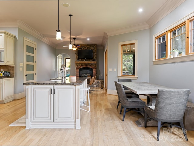 kitchen with backsplash, a center island with sink, sink, hanging light fixtures, and light hardwood / wood-style flooring