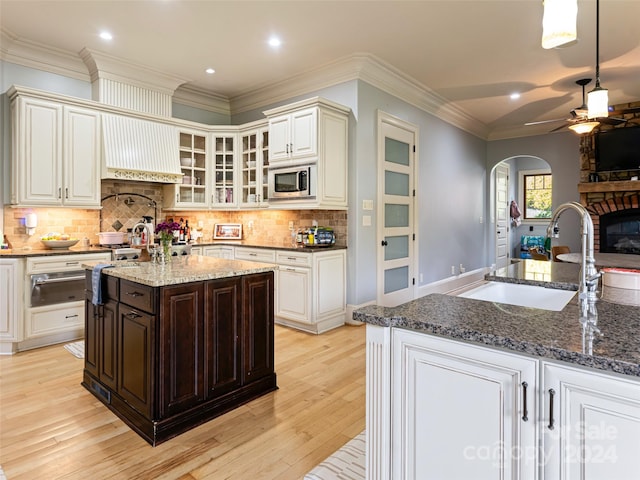 kitchen with crown molding, sink, a center island with sink, light hardwood / wood-style flooring, and stainless steel microwave