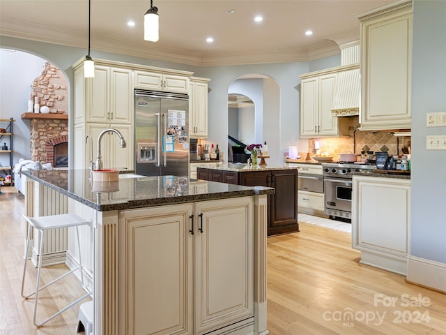 kitchen featuring light hardwood / wood-style flooring, cream cabinets, an island with sink, pendant lighting, and high end appliances