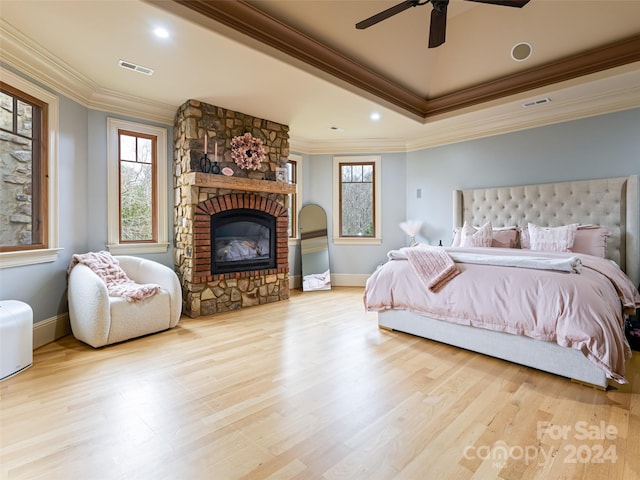 bedroom with light hardwood / wood-style floors, a stone fireplace, ceiling fan, and crown molding