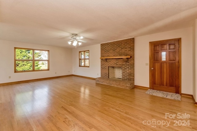 unfurnished living room featuring a textured ceiling, light wood-type flooring, a brick fireplace, and ceiling fan