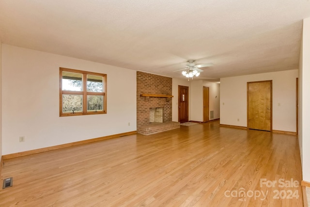 unfurnished living room with ceiling fan, a fireplace, a textured ceiling, and light wood-type flooring