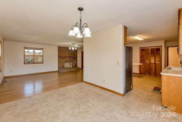 unfurnished living room with sink, light hardwood / wood-style floors, a textured ceiling, a fireplace, and ceiling fan with notable chandelier