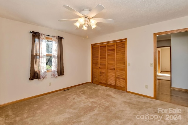 unfurnished bedroom featuring ceiling fan, a closet, light colored carpet, and a textured ceiling