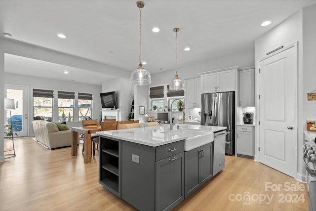 kitchen with appliances with stainless steel finishes, light hardwood / wood-style floors, gray cabinetry, and an island with sink