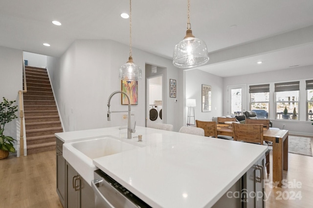 kitchen with washer and clothes dryer, sink, a center island with sink, light hardwood / wood-style floors, and hanging light fixtures