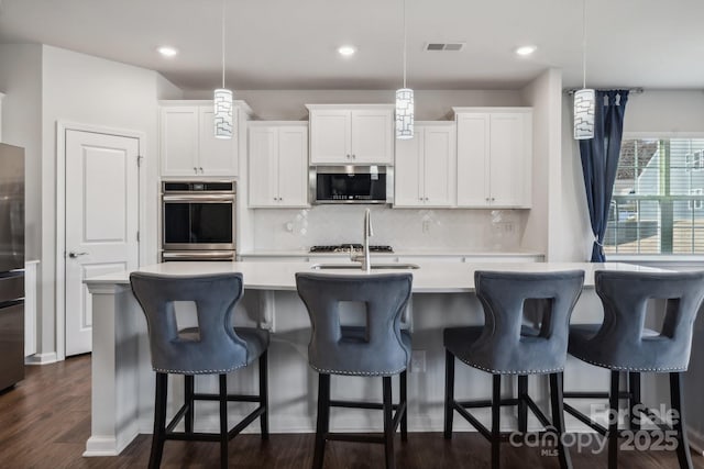 kitchen featuring a breakfast bar, white cabinets, an island with sink, appliances with stainless steel finishes, and decorative light fixtures