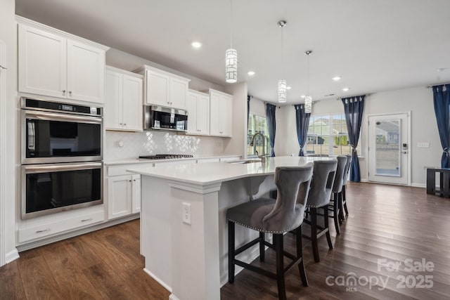 kitchen featuring a center island with sink, sink, appliances with stainless steel finishes, decorative light fixtures, and white cabinetry