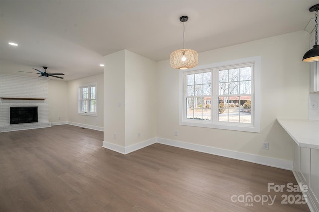 unfurnished dining area with ceiling fan, dark hardwood / wood-style floors, and a fireplace