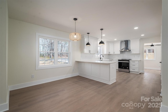 kitchen with decorative light fixtures, white cabinets, stainless steel range with electric stovetop, kitchen peninsula, and wall chimney range hood